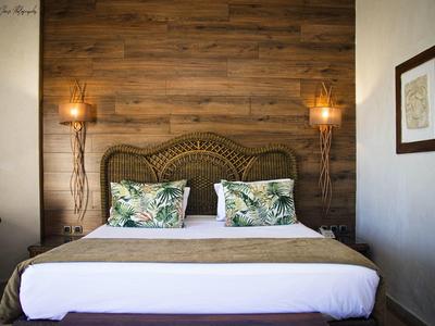Příjemná ložnice s dřevěnou zdí, ratanovým čelem postele a polštáři s tropickým motivem.