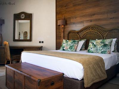 Pohodlný hotelový pokoj s dřevěným čelem postele, tropickými polštáři, velkou postelí a vintage truhlou u nohou.