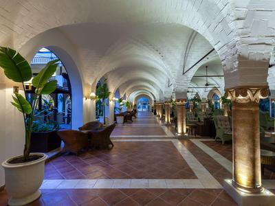 Ruime gewelfde gang met zuilen, planten en sfeerverlichting in een hotel.