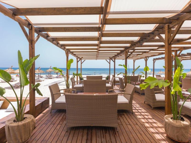 Venkovní posezení s ratanovým nábytkem a výhledem na moře pod dřevěnou pergolou.