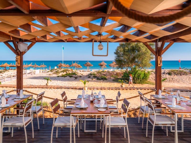 Un restaurant de plage couvert avec des tables donnant sur la mer et le ciel bleu.