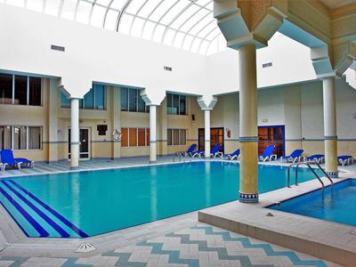 Piscina interna con sedie a sdraio e vasca idromassaggio nella hall coperta di un hotel.