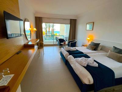 Camera d'hotel luminosa con due letti singoli, balcone con vista sulle palme e area salotto.