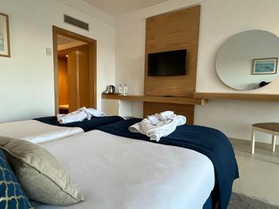 Camera d'hotel moderna con due letti singoli, TV a parete e grande specchio rotondo.