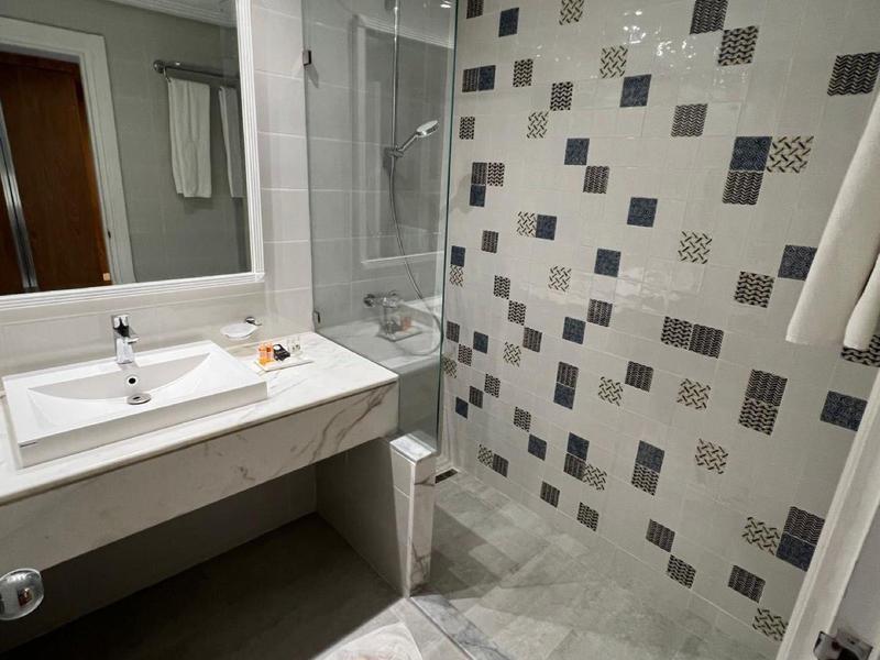 Bagno d'hotel moderno con lavabo bianco e doccia in vetro con parete decorata.