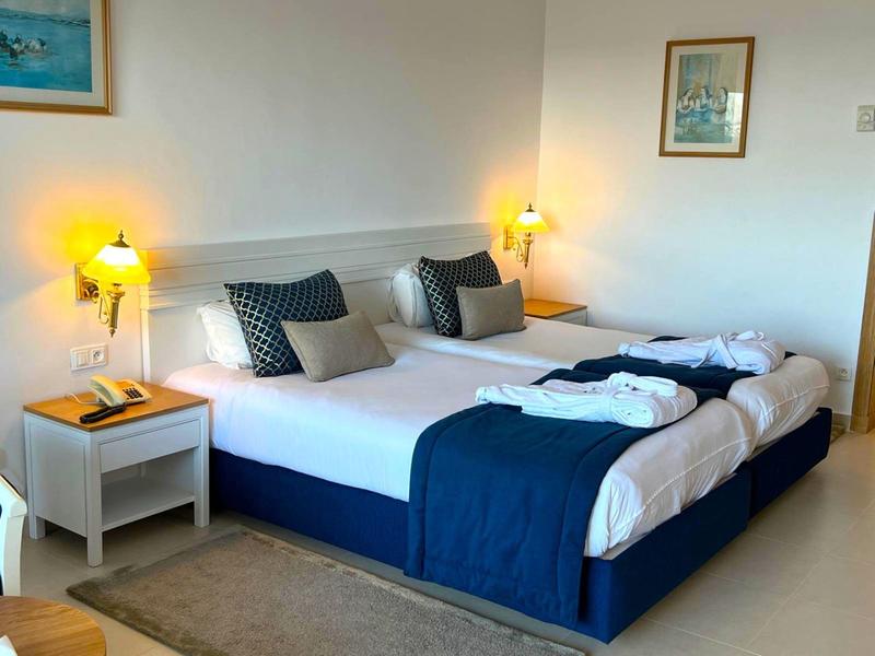 Camera d'hotel moderna con due letti singoli, coperte blu e lampade da comodino.