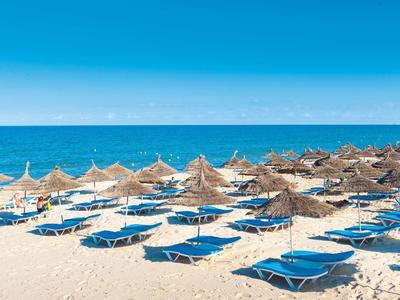Spiaggia di sabbia con lettini blu e ombrelloni di paglia sotto un cielo azzurro limpido vicino al mare