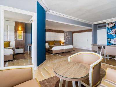 Camera d'hotel moderna con zona salotto, due letti e parete accentuata blu.