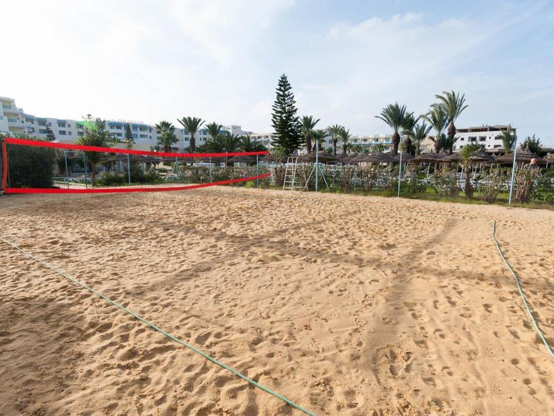 Grande campo di sabbia con rete da pallavolo e edifici sullo sfondo sotto un cielo nuvoloso