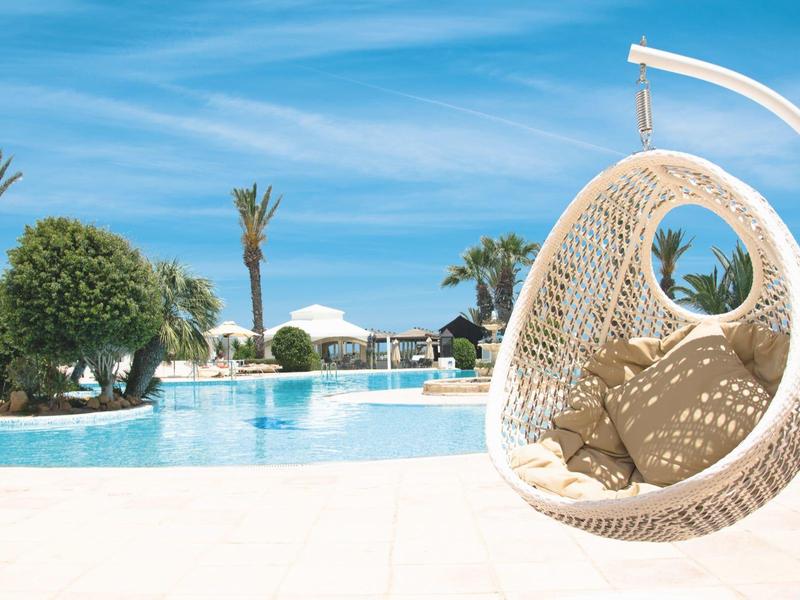 Piscina esterna moderna con sedia sospesa e palme in una giornata di sole