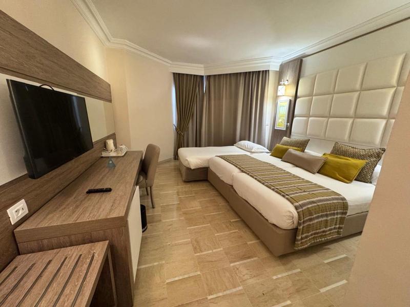 Camera d'hotel moderna con letto matrimoniale, scrivania, TV e grandi tende.