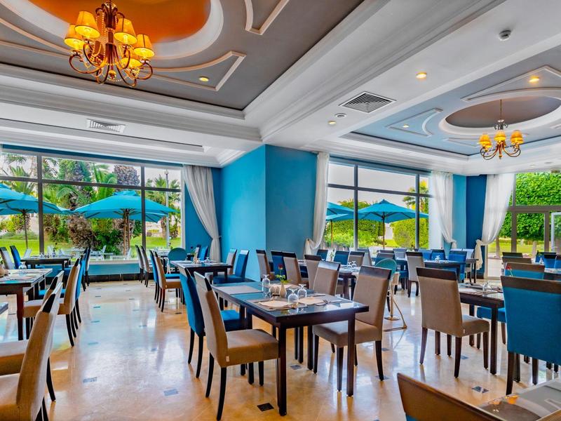 Ristorante luminoso con pareti blu, tavoli e sedie moderne e grandi finestre.