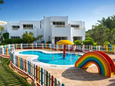 Kinderplanschbecken mit buntem Zaun und Regenbogen in einem Garten vor weißem Wohnhaus.