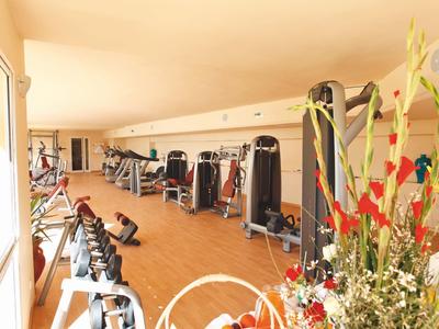 Großes Fitnessstudio mit verschiedenen Trainingsgeräten und hellen Holzböden.