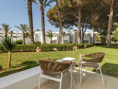 Dos sillas de jardín con una mesa pequeña en un césped frente a palmeras y arbustos.