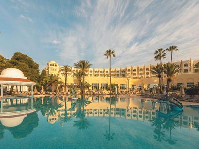 Grande hotel con piscina, palme e cielo azzurro al tramonto.