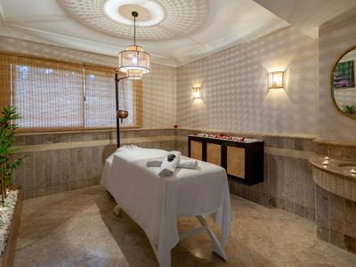 Stanza massaggi elegante con lettino, illuminazione soffusa e arredamento classico.