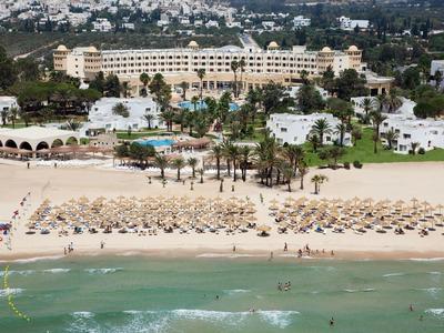 Strand mit Sonnenschirmen, Palmen und einem großen Hotel im Hintergrund am Meerufer.