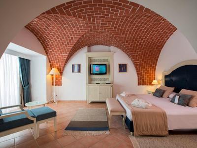 Gemütliches Schlafzimmer mit rotem Backstein-Gewölbe, Doppelbett, Sessel und weißem Schrank.