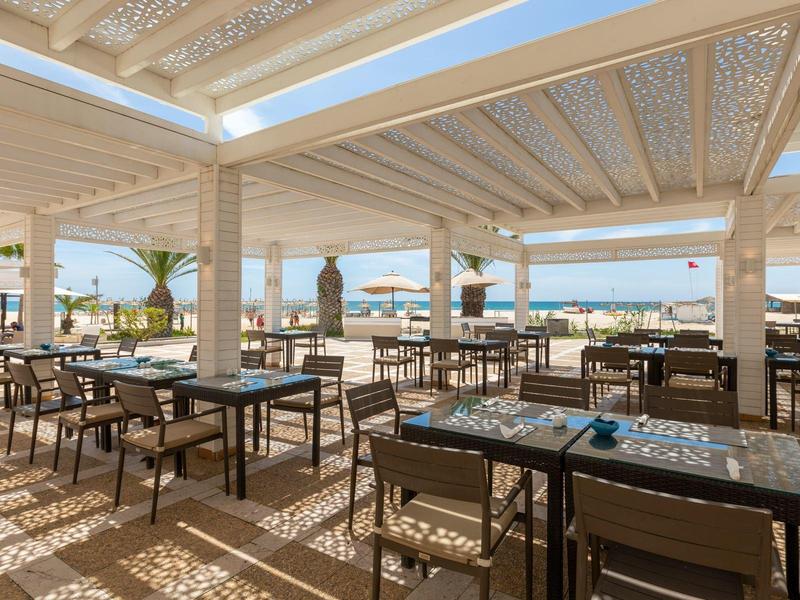 Terrazza ristorante coperta con vista mare, tavoli in legno e sedie.