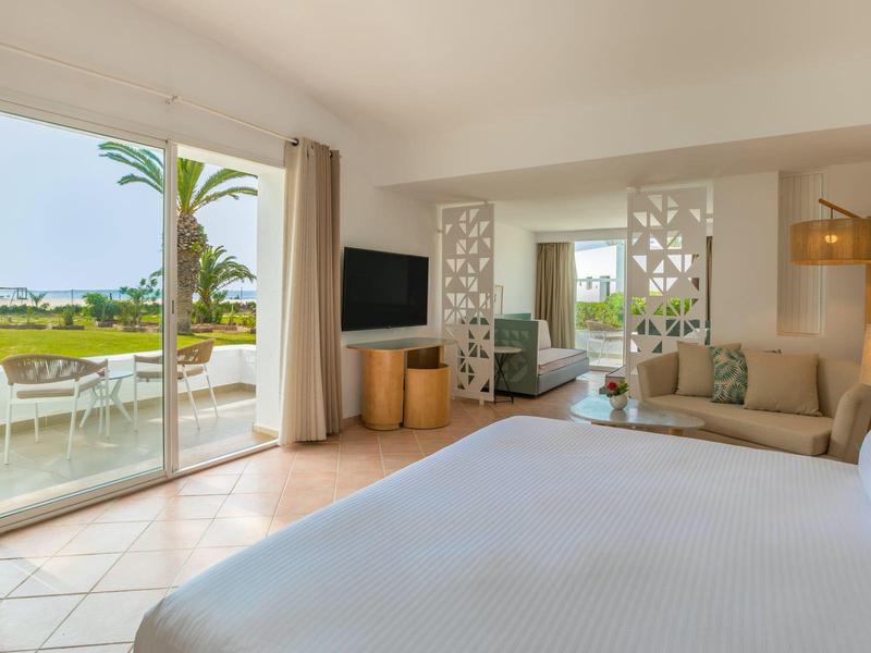 Camera luminosa con letto grande, divano, terrazza e vista su un giardino verde.