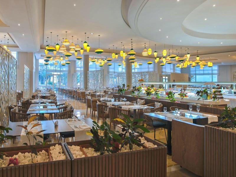 Ristorante elegante con grandi finestre, tavoli in legno e lampade gialle moderne.