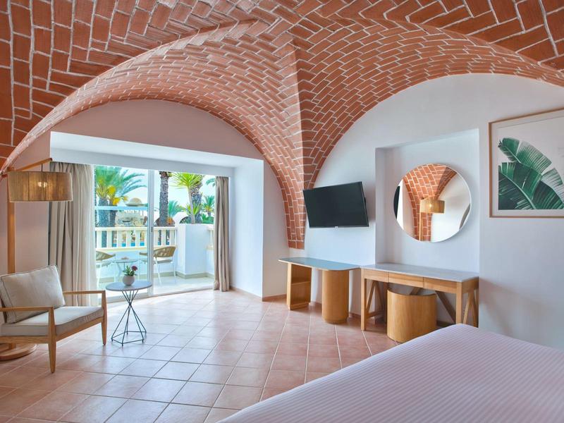 Camera luminosa con soffitto a volta in mattoni, ampia finestra e arredi moderni.