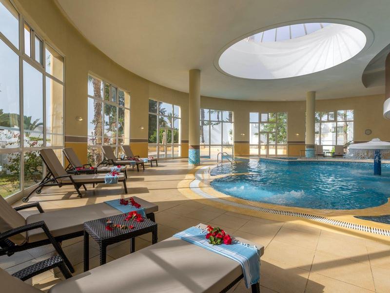 Piscina interna luminosa con sedie a sdraio e grandi finestre arcuate.