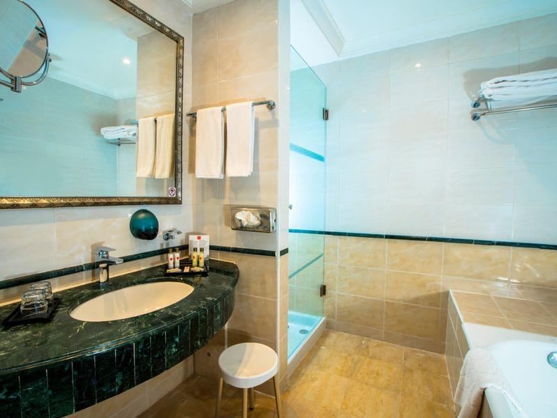 Bagno con lavandino in marmo, grande specchio, vasca da bagno e asciugamani bianchi.