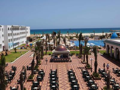 Grande complesso alberghiero con piscina all'aperto, palme e molti posti a sedere all'aperto vicino al mare.