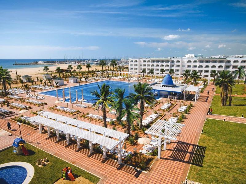 Grande resort con piscina, lettini e accesso diretto alla spiaggia sotto un cielo blu.