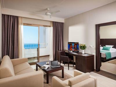 Modern hotel room with sea view, sofa, desk, and large mirror.