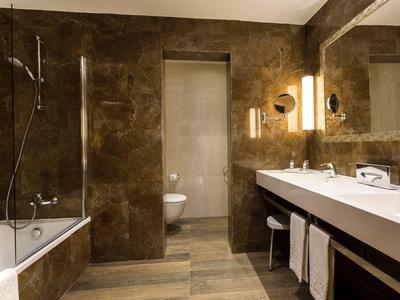 Modern bathroom with brown tiles, bathtub, sink, and illuminated mirror.