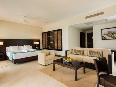 Modern furnished hotel room with bed, sofa, armchairs, and a table with flowers.