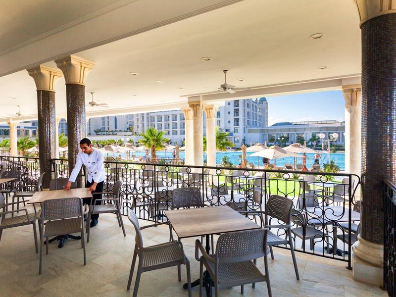 Covered hotel terrace with tables, chairs, and a view of the pool and sea.