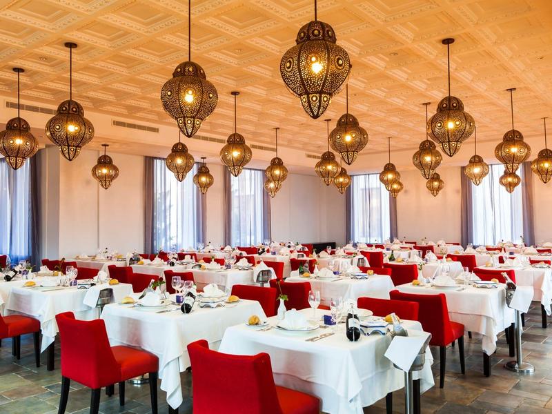 Elegant restaurant with red chairs and white tablecloths, lit by decorative chandeliers.