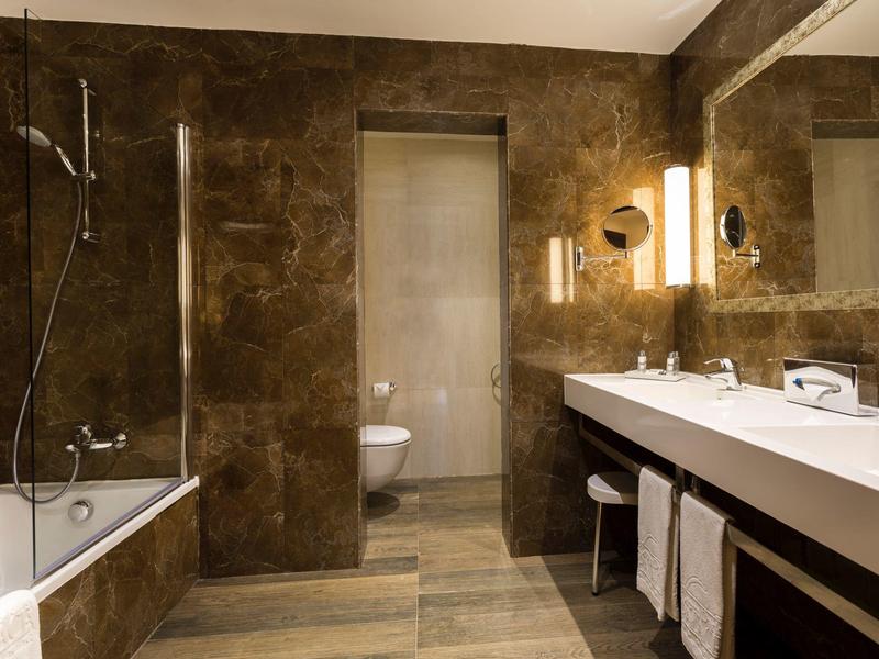 Modern bathroom with brown tiles, bathtub, sink, and illuminated mirror.