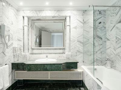 Helles Badezimmer mit weißen Marmorfliesen, großem Spiegel, schwarzer Waschtischplatte und Badewanne.