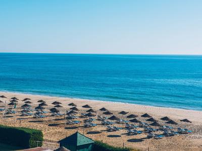 Strand mit Reihen von Sonnenschirmen und Blick auf das klare blaue Meer unter klarem Himmel.