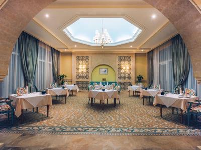 Eleganter Speisesaal mit runden und rechteckigen Tischen, blauen Vorhängen und Kronleuchter.