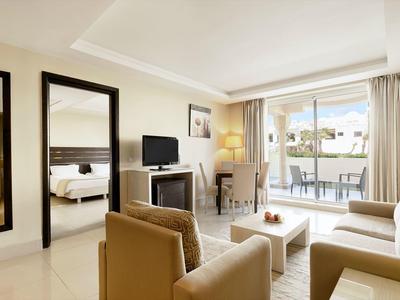 Modern eingerichtetes Hotelzimmer mit Sitzbereich, Balkon und Blick auf den Pool.