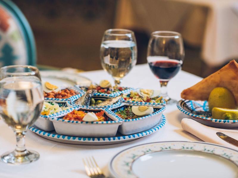 Ein gedeckter Tisch mit bunten Snacks, Wassergläsern und einem Teller mit Brot und Gurkenscheiben.