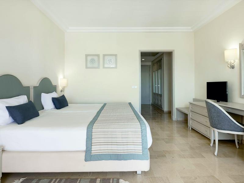 Helles, modernes Schlafzimmer mit Doppelbett, zwei Kissen, Fernseher und Schreibtisch mit Spiegel.