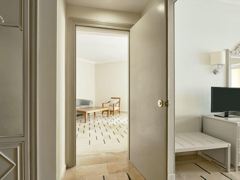 Blick durch eine geöffnete Tür in ein helles Zimmer mit Holzstuhl und Teppich.