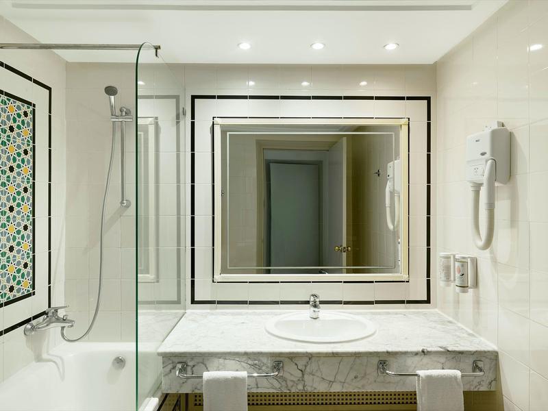 Moderner Hotelbadezimmer mit Spiegel, Waschbecken und Badewanne mit Glaswand.