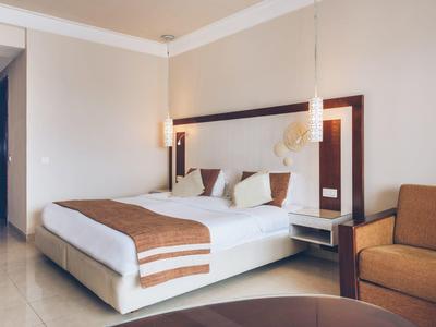 Modernes Hotelzimmer mit großem Bett, zwei Nachtlampen und braunem Sessel.