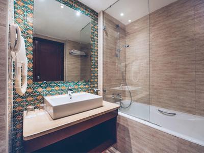 Modernes Hotelbadezimmer mit Waschbecken, großem Spiegel und Badewanne mit Glasabtrennung.