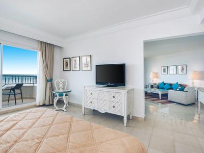 Hell eingerichtetes Hotelzimmer mit Balkon und Meerblick, angrenzendem Wohnzimmer und bequemen Möbeln.