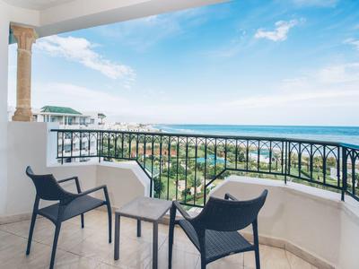 Balkon mit zwei schwarzen Stühlen, kleinem Tisch und Blick auf das Meer bei klarem Himmel.