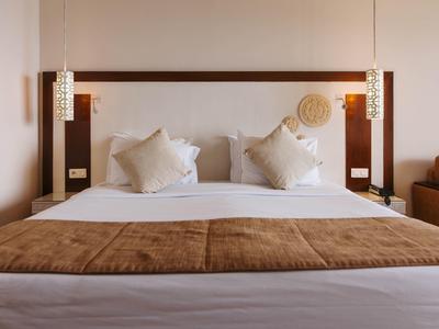 Modernes Hotelzimmer mit großem Bett, weißen Kissen und brauner Bettdecke.